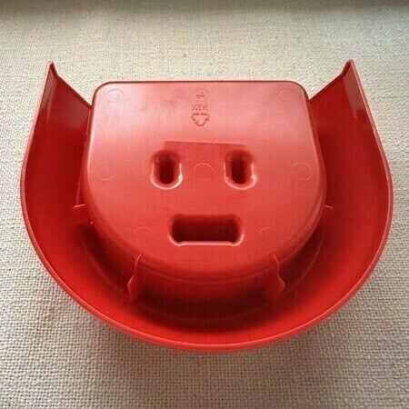 A red plastic cut out with a face-like design.
Una pieza de plástico rojo con un diseño que parece una cara.
Plastikozko pieza gorri bat, aurpegi itxurako diseinua duena.